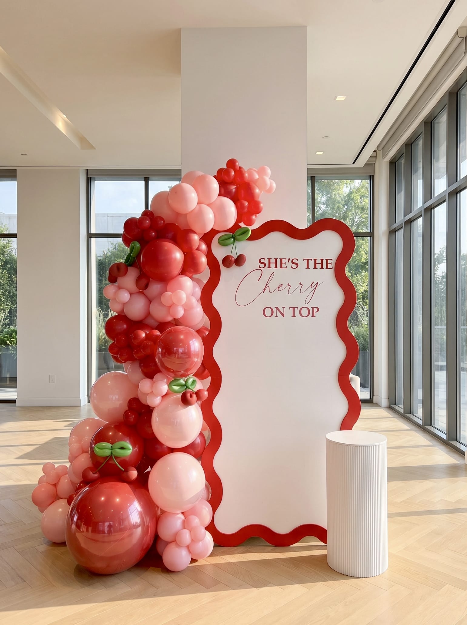 Cherry-themed birthday backdrop featuring a white wavy panel with red border, custom lettering, pink and red balloon garland, cherry accents, and a white ribbed pedestal stand.