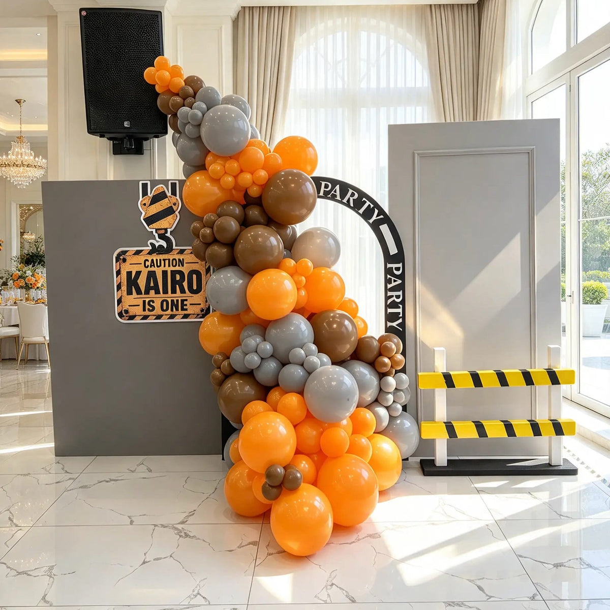 Construction birthday setup with grey panels, orange and brown balloons, a personalized caution sign, road arch, and striped barrier.