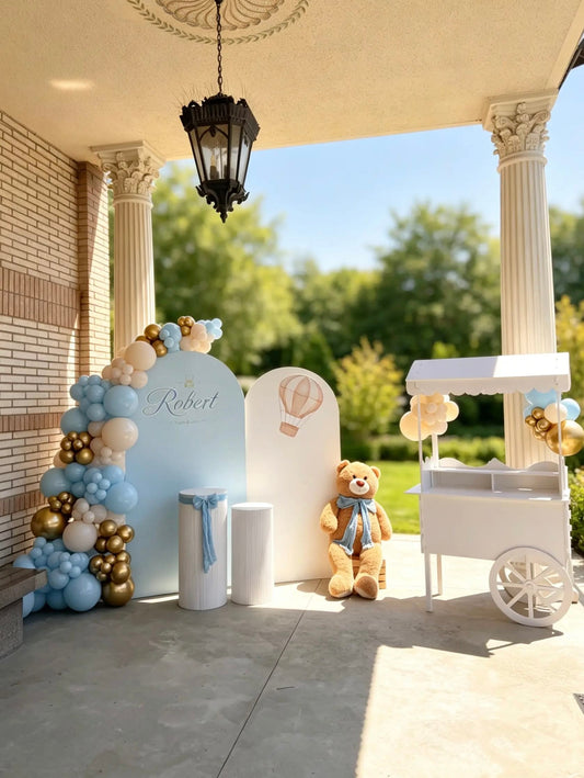 Teddy bear christening backdrop with baby blue, ivory and gold balloons, custom panels, cake tables and white candy cart.